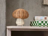 En lille kurvlampe formet som en svamp står på en træhylde ved siden af to farverige rektangulære kasser foran en grå væg.