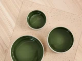Tre grønne skåle i forskellige størrelser er anbragt på en beige, plettet måtte, der ligger på en lys træoverflade, set ovenfra.