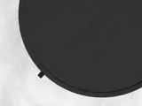 Et nærbillede af en rund, sort bordplade med træstruktur på en lysegrå, struktureret baggrund. Kun en del af bordet er synligt i øverste højre hjørne.