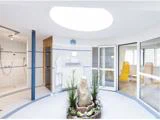 Et lyst, moderne spa-rum med klinkegulv, åbent bruseområde, liggestole i et solrum og en central indendørs stenhave med planter under et stort rundt ovenlys.