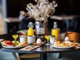 Et morgenbord med kager, toast, frugt, kogte æg, juice, en fransk presse, kaffekopper og en vase med tørrede blomster i midten.