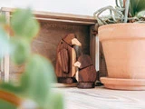To pingvinfigurer i træ sidder ved siden af en terrakottapotteplante i en rustik trækasse på en lys træoverflade.