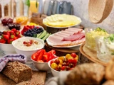 Et morgenmadsbord med et udvalg af frugt, pålæg, oste, brød, dip og grøntsager, der er anrettet på et bord.
