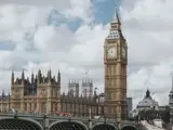 Billedet viser Londons klokketårn Big Ben og Palace of Westminster med en overskyet himmel og mennesker, der krydser Westminster Bridge.