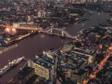 Luftfoto af London om natten med den oplyste Tower Bridge over Themsen og de omkringliggende bygninger med lys.
