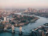 Luftfoto af London med Tower Bridge over Themsen, med byens bygninger og Canary Wharf skyline i det fjerne.
