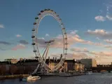 Pariserhjulet London Eye ved Themsen med både på vandet og bygninger i baggrunden under en delvis overskyet himmel ved solnedgang.
