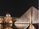 Louvre-museets oplyste glaspyramide står ved siden af den historiske bygning om aftenen og spejler sig i vandet nedenunder.