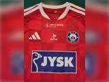 Rød fodboldtrøje med ternet mønster, JYSK-logoet, Silkeborg IF’s klubvåben, et Lars Larsen Group-logo og et mærke fra arrangementet Veteran Match.