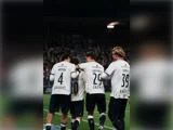 Fire fodboldspillere i hvidstribede trøjer, der fejrer et mål på banen.