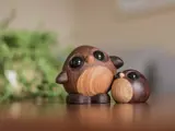To uglefigurer af træ med store sorte øjne sidder på en glat overflade med en grøn, sløret baggrund.