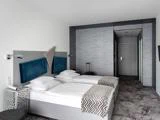 Moderne hotelværelse med to enkeltsenge skubbet sammen, hvidt sengetøj, blå sengegavle, mønstrede tæpper, et lille bord og en kuffert ved døren.