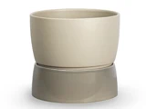 En beige keramikpotte står oven på en lidt bredere, grå keramikunderkop på en hvid baggrund.