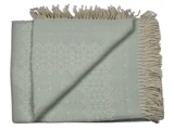 Et foldet lysegrønt vævet tæppe med et diskret geometrisk mønster og cremefarvede frynser langs den ene kant.
