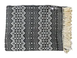 Et foldet sort og hvidt mønstret tæppe med geometriske mønstre og cremefarvede frynser på den ene kant.