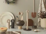En moderne køkkenscene med træredskaber i en vase, keramiske beholdere, en udskåret melon, tallerkener og minimalistisk indretning på en marmorbordplade mod en beige væg.