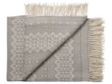 Et foldet gråt og hvidt mønstret vævet tæppe med frynsede kanter, delvist udfoldet for at vise det dekorative geometriske design.