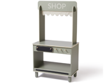 En lille, lysegrå legebutik i træ med baldakin, en åben hylde, knopper og en skuffe, hvor der står SHOP på skiltet øverst.