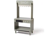 En lille, lysegrå legebutik i træ med baldakin, en åben hylde, knopper og en skuffe, hvor der står SHOP på skiltet øverst.