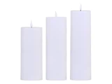Tre hvide bloklys i forskellige højder med små flammer, anbragt side om side på en hvid baggrund.