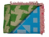 Et foldet tæppe med grønne og beige geometriske mønstre på den ene side, blå og beige former på den anden side og frynsede rosa kanter.