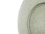 Et nærbillede af en struktureret, plettet rund plade med en metallisk eller keramisk finish, der kun viser en del af overfladen mod en hvid baggrund.