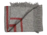 Et foldet gråt uldtæppe med røde striber og frynsede kanter, sirligt arrangeret på en hvid baggrund.