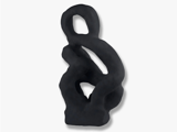 Abstrakt sort skulptur med glatte, buede former og en løkke i toppen, som står på en almindelig hvid baggrund.