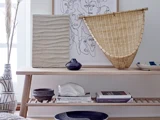 Et konsolbord i træ med kunst, en rottingkurv, vaser, bøger og keramikudsmykning i en minimalistisk, moderne bolig.