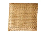 En firkantet, flettet strå- eller kurvemåtte eller -pude med en naturlig lysebrun farve på en hvid baggrund.