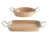 To bageforme af glas, en rund og en rektangulær, hver placeret i flettede rottingkurve med håndtag på begge sider, på en hvid baggrund.