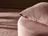 Et nærbillede af en blød, pink, rund skammel med en matchende perforeret pude på toppen, badet i varmt, naturligt lys.