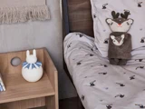 Børneseng med sengetøj med dyreprint, en plyshjort og koala-legetøj og et natbord i træ med en hvid kaninlampe og bøger.