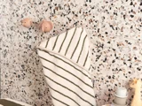 Et stribet håndklæde hænger på terrazzo-vægkroge formet som dyreansigter over toiletsager og en lille giraffigur.