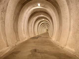 En lang, buet tunnel med jævnt fordelte, afrundede buer og ovenlys, alt sammen i et beige, betonlignende materiale.