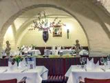 En hyggelig restaurant med buede lofter, hvide duge, pænt opstillede borde, elegante glas og en høj vase med lyserøde blomster som midtpunkt.