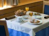 Et lille bord til to dækket med croissanter, en brødkurv, frugt, en kop kaffe, appelsinjuice og vin i en lys spisestue.