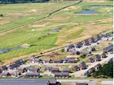 Luftfoto af et boligkvarter med røde murstenshuse ved siden af en stor grøn golfbane med damme og sandfang.