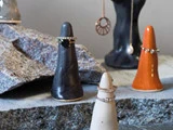 Tre keramiske ringholdere - sort, orange og hvid - viser ringe på en stenoverflade med smykker og flere holdere synlige i baggrunden.