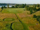 Luftfoto af en golfbane med to tee-bokse, en green, sandbunkere, omgivende træer og en sø i baggrunden.