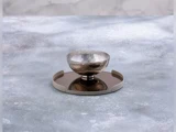 En riflet sølvskål står på en reflekterende brun bakke med en lysegrå kant mod en grå struktureret baggrund med skygger.