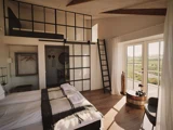 Et moderne, solrigt soveværelse med hems, store glasvinduer, trægulv, dobbeltseng og en stige, der fører op til øverste etage.