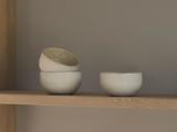Tre små hvide keramikskåle på en træhylde; to er stablet med den øverste på skrå, og en skål står for sig selv.