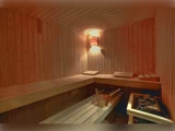 Saunarum i træ med bænke i flere niveauer, en spand og øse i træ og en vægmonteret lampe, der skaber en varm og hyggelig atmosfære.