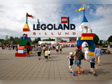 Folkemængder strømmer ind gennem den farverige hovedindgang til LEGOLAND Billund, der er prydet med LEGO-inspirerede buer og tårne under en overskyet himmel.