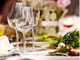 Et nærbillede af et bord med tomme vinglas, hvide servietter og tallerkener med frisk salat, med en let sløret baggrund, der antyder en formel spisesituation.