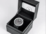 Et sort armbåndsur med grønne timemarkeringer i en sort gaveæske, ledsaget af et kort med logoet SW på indersiden af låget.