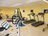 Et fitnesscenter med løbebånd, motionscykel, vægte, bænke, stabilitetsbolde og gule vægge dekoreret med sort-hvide fitnessbilleder.