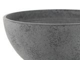 Nærbillede af en struktureret, mørkegrå keramikskål mod en hvid baggrund. Kun en del af skålen er synlig.