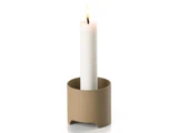 Et tændt hvidt stearinlys står oprejst i en enkel, rund, beige lysestage mod en almindelig hvid baggrund.